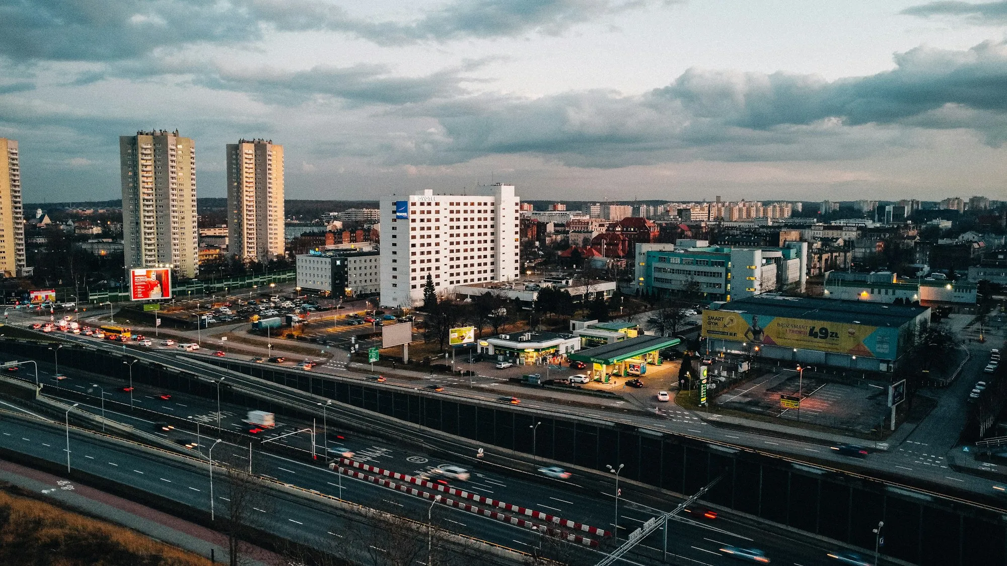 Widok miasta o zmierzchu z widocznymi nośnikami reklamy zewnętrznej przy ruchliwej ulicy